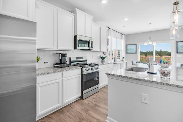 kitchen featuring stainless steel appliances, backsplash, decorative light fixtures, white cabinets, and sink