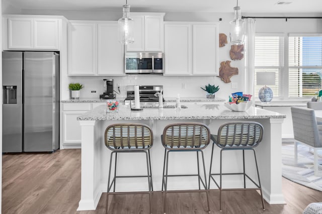 kitchen with a center island with sink, stainless steel appliances, white cabinets, and decorative light fixtures