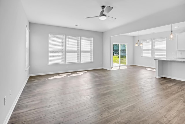 unfurnished living room with dark hardwood / wood-style floors, a wealth of natural light, and ceiling fan with notable chandelier