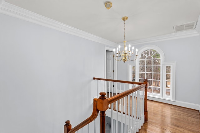 staircase with wood-type flooring, ornamental molding, and an inviting chandelier