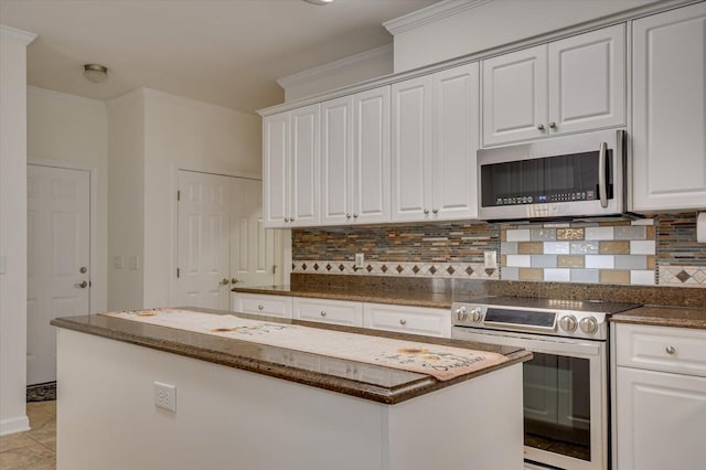 kitchen featuring stainless steel appliances, white cabinetry, ornamental molding, backsplash, and dark stone counters