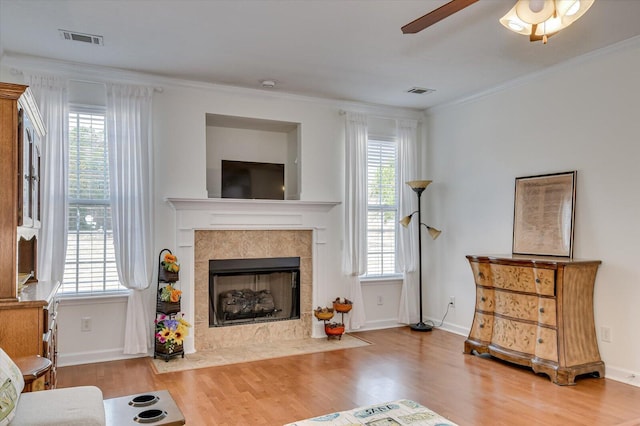 living area featuring a tile fireplace, visible vents, light wood-style floors, a healthy amount of sunlight, and crown molding