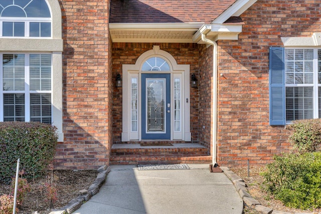 view of exterior entry featuring brick siding and roof with shingles