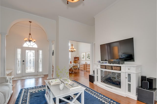 living room with arched walkways, wood finished floors, ornamental molding, an inviting chandelier, and ornate columns