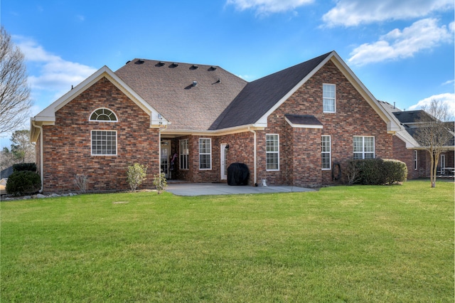 rear view of property featuring a yard, brick siding, a patio, and roof with shingles