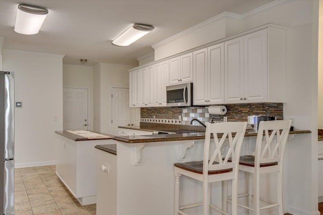 kitchen with tasteful backsplash, white cabinets, dark countertops, appliances with stainless steel finishes, and a peninsula