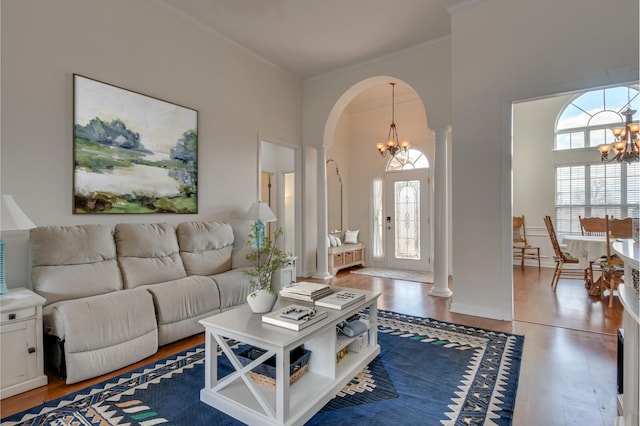 living area with arched walkways, a notable chandelier, wood finished floors, a wealth of natural light, and decorative columns