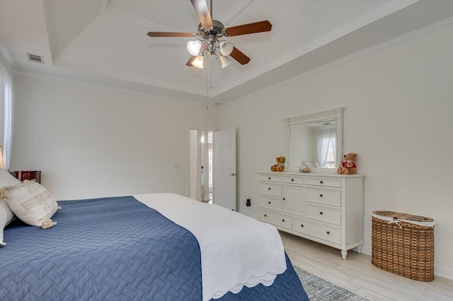 bedroom with visible vents, a ceiling fan, ornamental molding, light wood-type flooring, and a raised ceiling