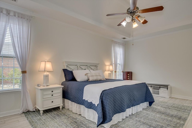 bedroom with baseboards, visible vents, ceiling fan, a tray ceiling, and light wood-style floors