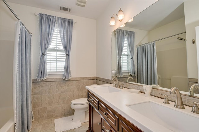 bathroom featuring toilet, tile walls, visible vents, and a sink