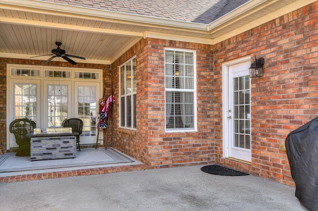 doorway to property featuring brick siding, ceiling fan, and roof with shingles