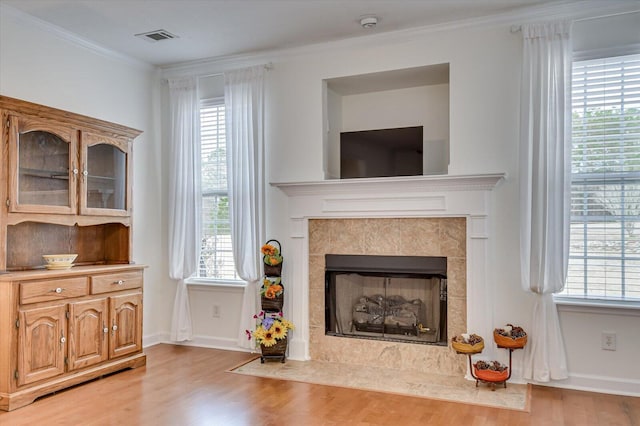 living area with light wood-style flooring, a fireplace, visible vents, a wealth of natural light, and crown molding