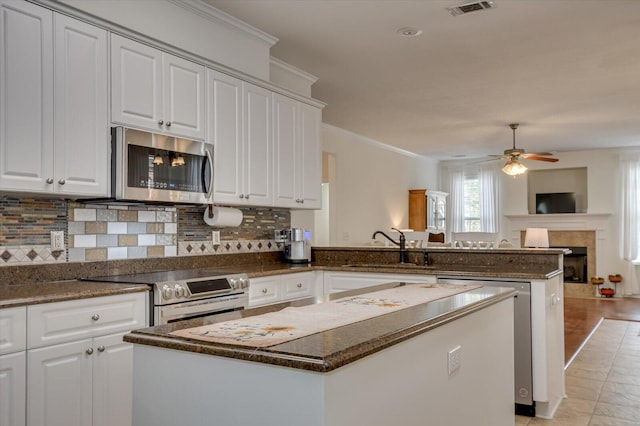 kitchen featuring a kitchen island, appliances with stainless steel finishes, a fireplace, white cabinetry, and a sink