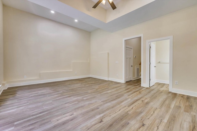 empty room with ceiling fan, light hardwood / wood-style floors, and a towering ceiling