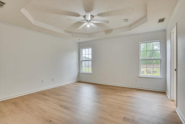 empty room featuring a tray ceiling, light hardwood / wood-style flooring, and a textured ceiling