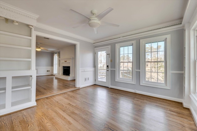 unfurnished living room featuring crown molding, ceiling fan, built in shelves, and light hardwood / wood-style floors