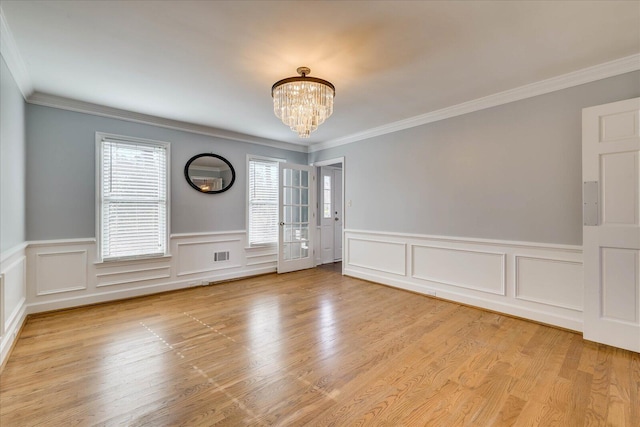 empty room with ornamental molding, an inviting chandelier, and light hardwood / wood-style floors