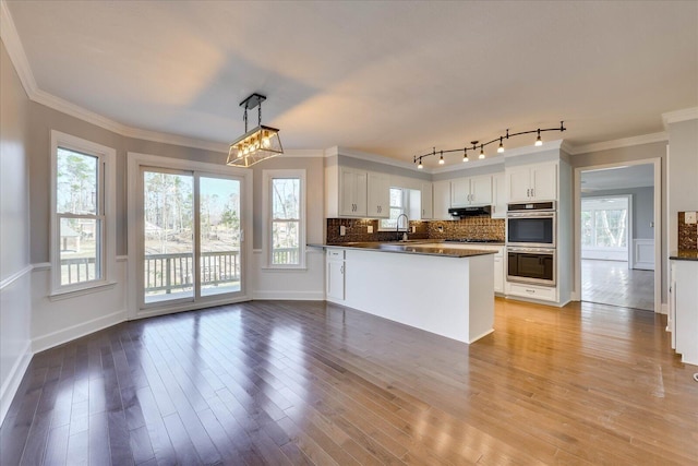 kitchen with stainless steel double oven, kitchen peninsula, white cabinets, and decorative light fixtures