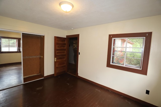 unfurnished bedroom with multiple windows, dark wood-type flooring, a closet, and a textured ceiling