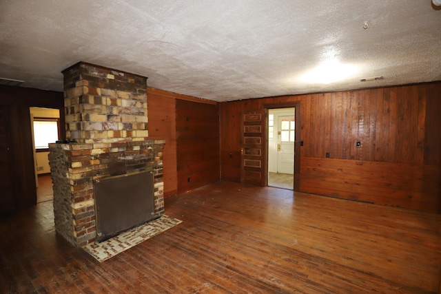 unfurnished living room featuring dark wood-type flooring, a textured ceiling, a fireplace, and wooden walls