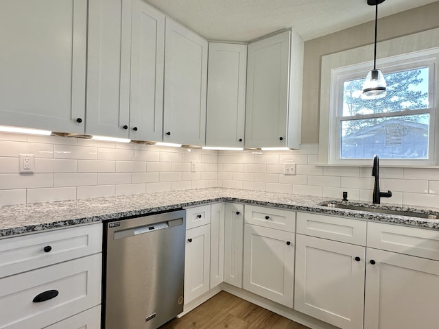 kitchen featuring light wood-type flooring, a sink, tasteful backsplash, stainless steel dishwasher, and white cabinetry