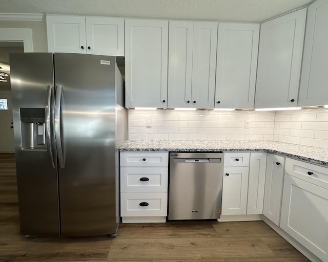 kitchen with white cabinets, light stone countertops, stainless steel appliances, and wood finished floors