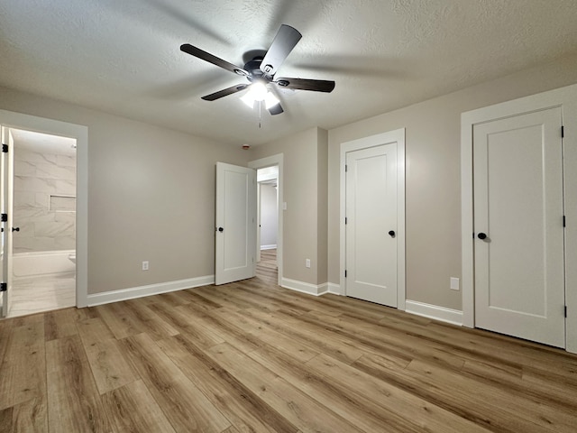 unfurnished bedroom featuring a ceiling fan, ensuite bathroom, a textured ceiling, light wood finished floors, and baseboards