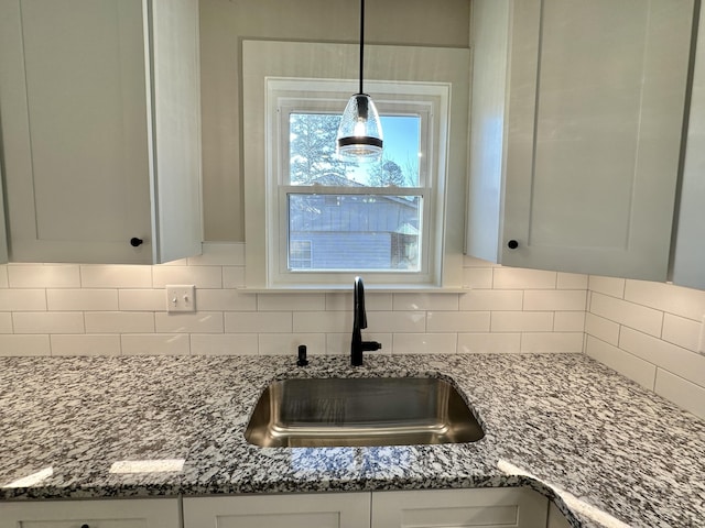 kitchen featuring decorative backsplash, hanging light fixtures, stone counters, and a sink