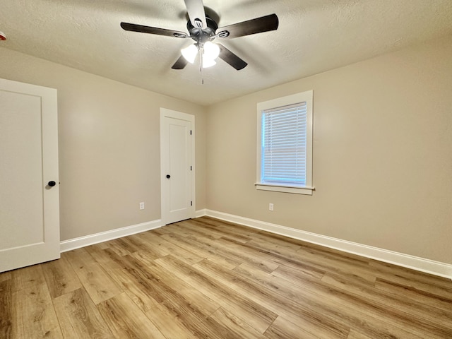 spare room with a ceiling fan, baseboards, light wood finished floors, and a textured ceiling