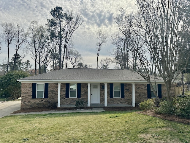 ranch-style home with a front yard, covered porch, brick siding, and roof with shingles