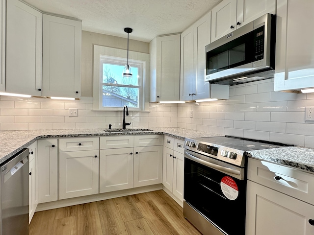 kitchen featuring appliances with stainless steel finishes, white cabinetry, light wood-style floors, and a sink