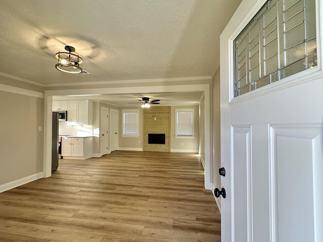 unfurnished living room with ceiling fan, a fireplace, light wood-style flooring, and crown molding