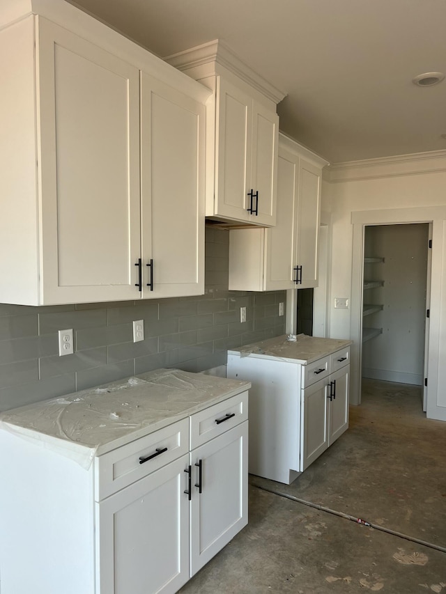 kitchen featuring light stone counters, white cabinets, ornamental molding, decorative backsplash, and unfinished concrete floors