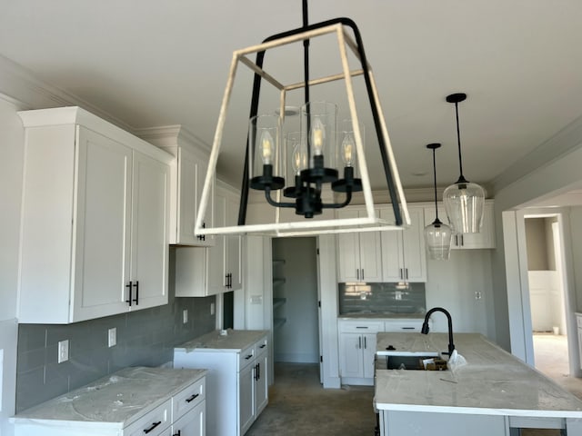 kitchen featuring a chandelier, a sink, ornamental molding, light stone countertops, and a center island with sink