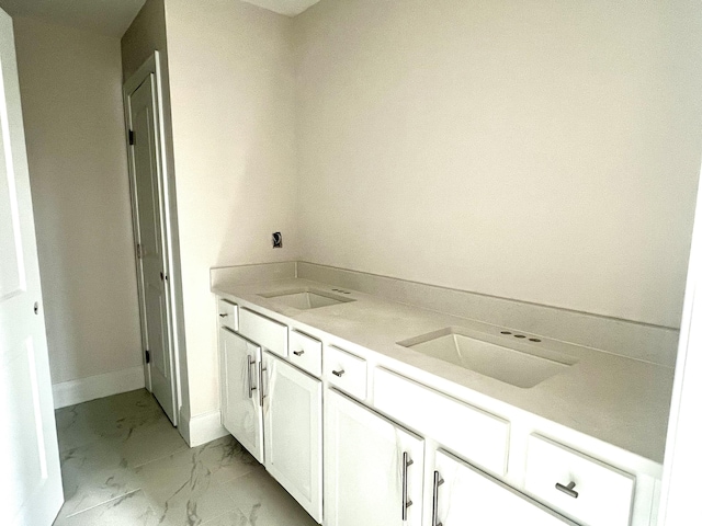 full bathroom featuring double vanity, marble finish floor, baseboards, and a sink