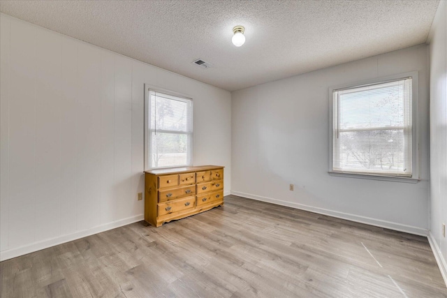 empty room featuring light wood-style floors, baseboards, visible vents, and a textured ceiling