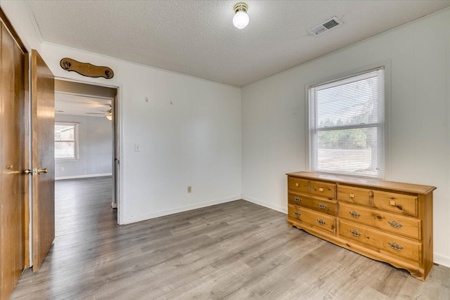 unfurnished room with a textured ceiling, light wood-style flooring, and visible vents