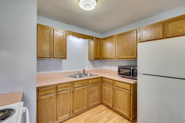 kitchen featuring a sink, light countertops, freestanding refrigerator, light wood finished floors, and stainless steel microwave