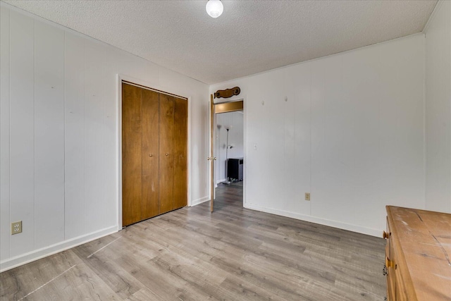 unfurnished bedroom with a textured ceiling, light wood finished floors, a closet, and baseboards