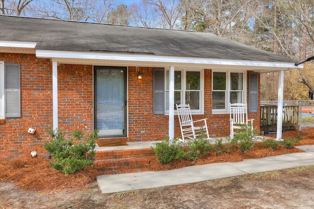 property entrance featuring a shingled roof, covered porch, and brick siding