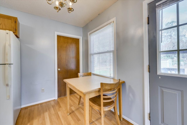 dining area with light wood-style floors, a notable chandelier, a textured ceiling, and baseboards