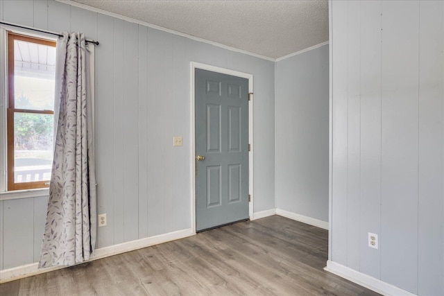 unfurnished room with crown molding, a textured ceiling, baseboards, and wood finished floors