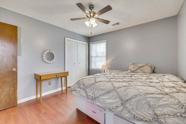 bedroom featuring a closet, visible vents, a textured ceiling, wood finished floors, and baseboards