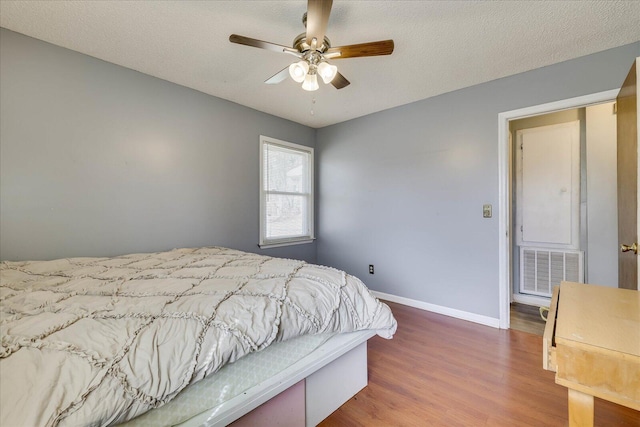 bedroom featuring visible vents, a textured ceiling, baseboards, and wood finished floors