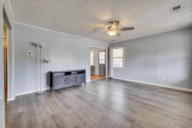 unfurnished living room featuring wood finished floors, visible vents, baseboards, a ceiling fan, and ornamental molding