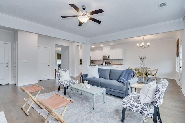 living area with a ceiling fan, wood finished floors, a chandelier, baseboards, and crown molding