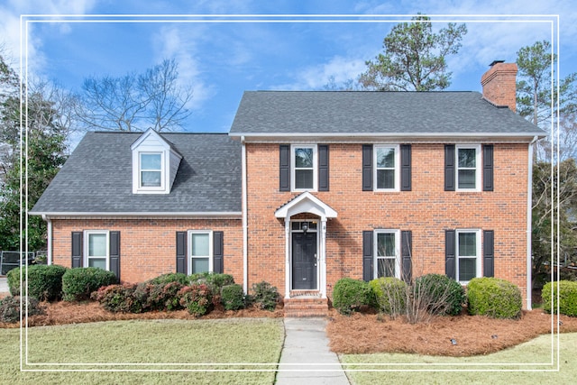 colonial-style house featuring brick siding, a chimney, and a front lawn