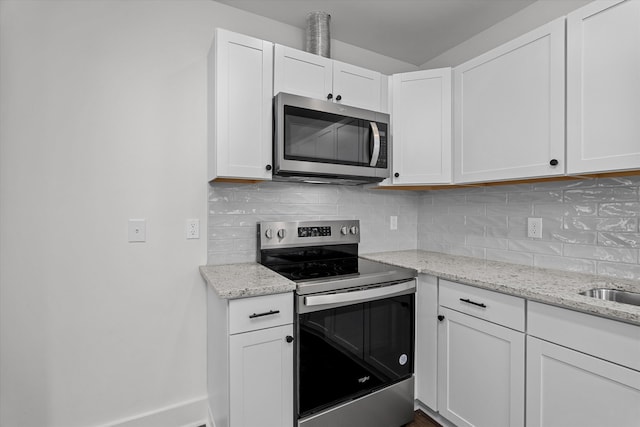 kitchen with stainless steel appliances, tasteful backsplash, light stone counters, and white cabinets