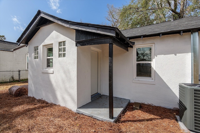 view of property exterior featuring a shingled roof, stucco siding, fence, and central air condition unit