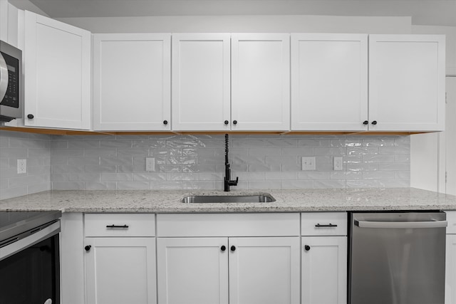 kitchen featuring light stone counters, stainless steel appliances, decorative backsplash, white cabinets, and a sink